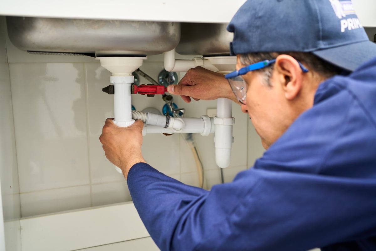 Plumbing, handyman and maintenance with man in kitchen for repair, industrial and inspection. Pipes, tools and safety with male plumber fixing sink for home improvement, drainage and water system